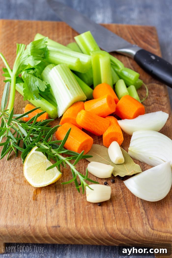 Chopped vegetables (celery, carrots, onion) and herbs (rosemary, bay leaves) on a wooden cutting board.