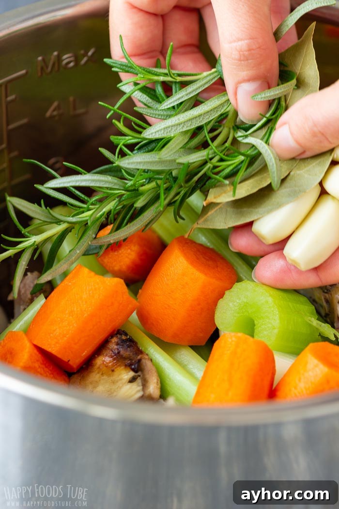 Julia holding fresh herbs and garlic over a pot filled with chopped carrots, celery, and other vegetables.