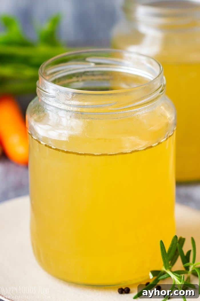 A large jar filled with clear, golden turkey stock with herbs and vegetables in the background.
