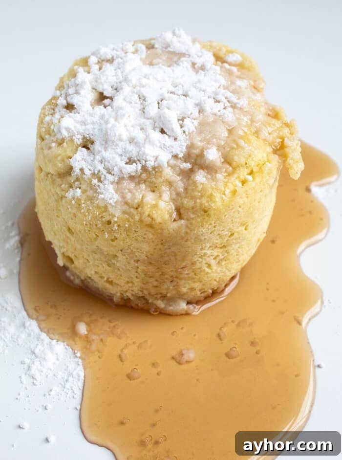 keto pancake mug cake on a white background with maple syrup all around it