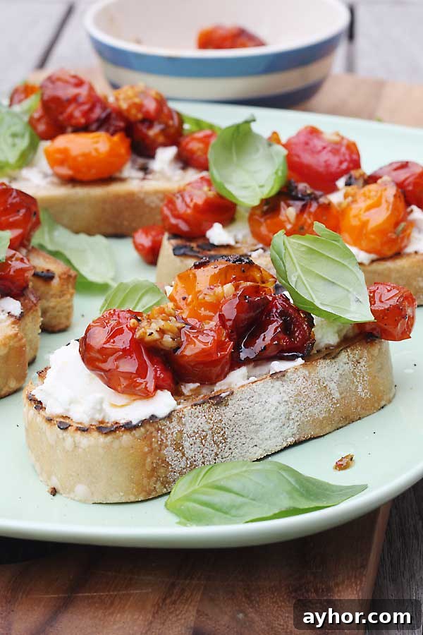 A closeup of a piece of toast with ricotta, tomatoes and basil on it on a white plate.