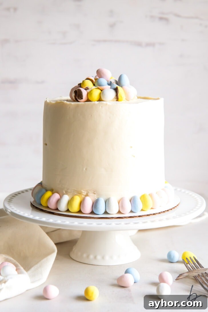white cake stand holding a cadbury mini egg cake with buttercream frosting and pastel easter egg candies for garnish