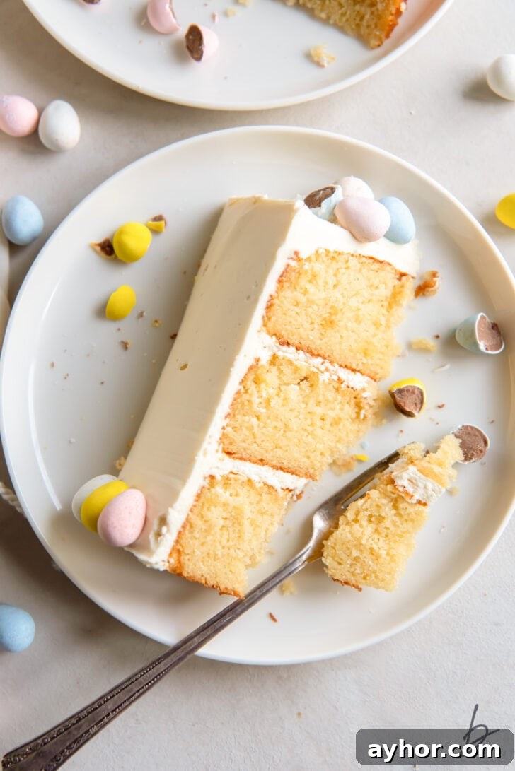 Cadbury mini egg cake slice with a few pastel chocolate eggs on white plate and fork taking a bite of cake
