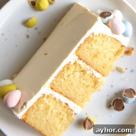 slice of triple layer cadbury mini egg cake with vanilla frosting on a plate with broken chocolate mini eggs
