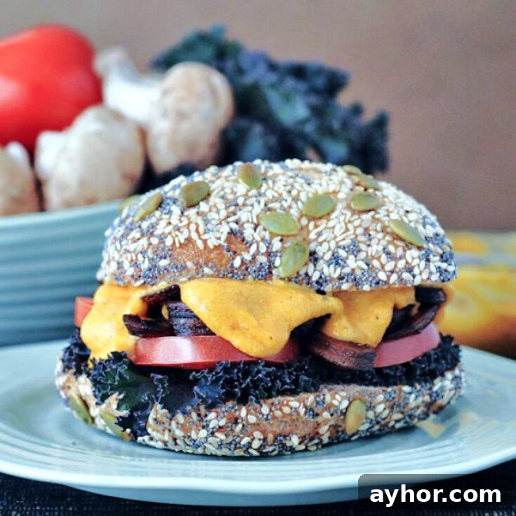 A mushroom melt sandwich with curly kale, tomato slices, mushrooms and cheese sauce on a seeded bun.