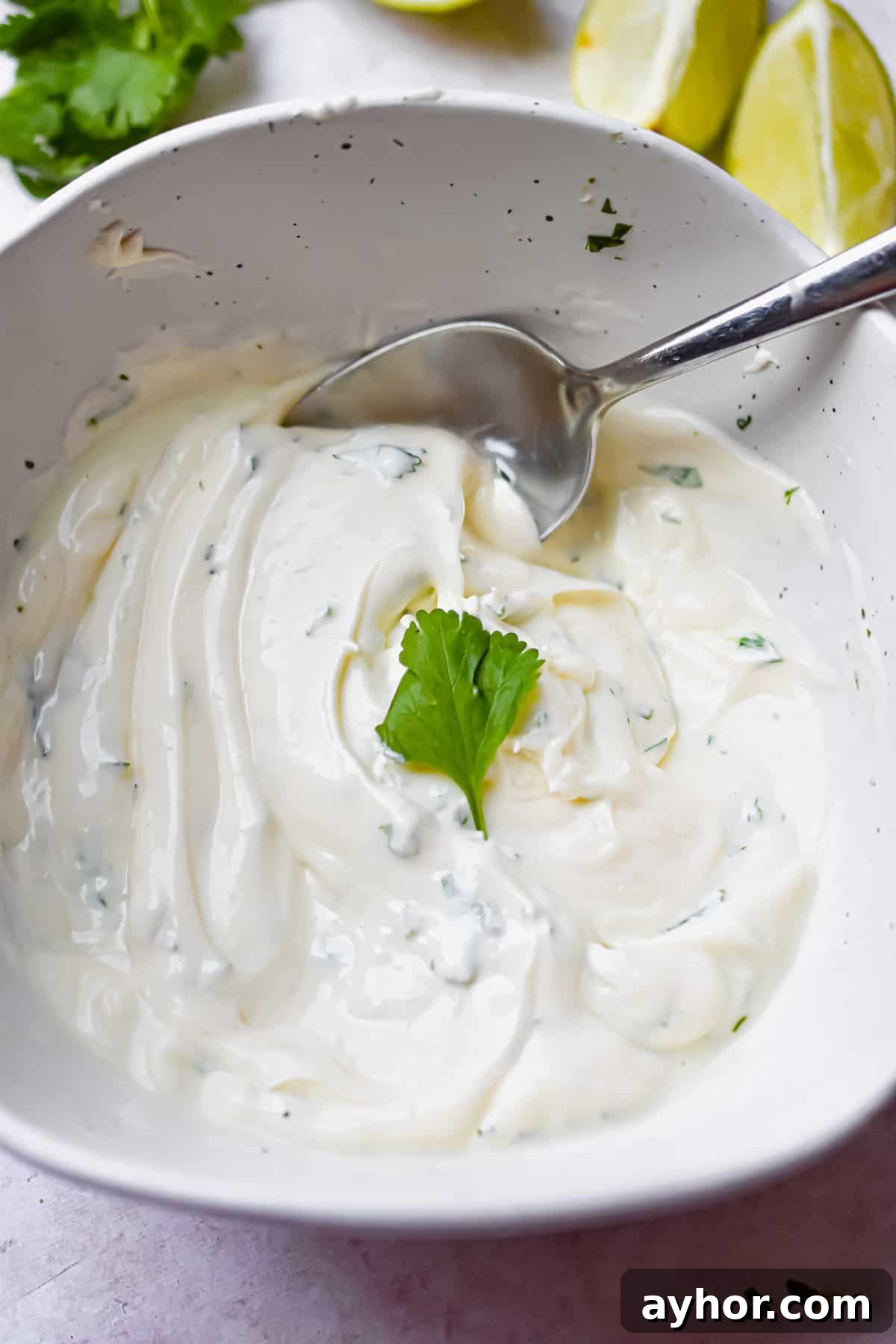 A spoon is in the bowl with limes and cilantro in the background