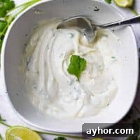 A bowl of cilantro lime aioli is surrounded by limes and cilantro