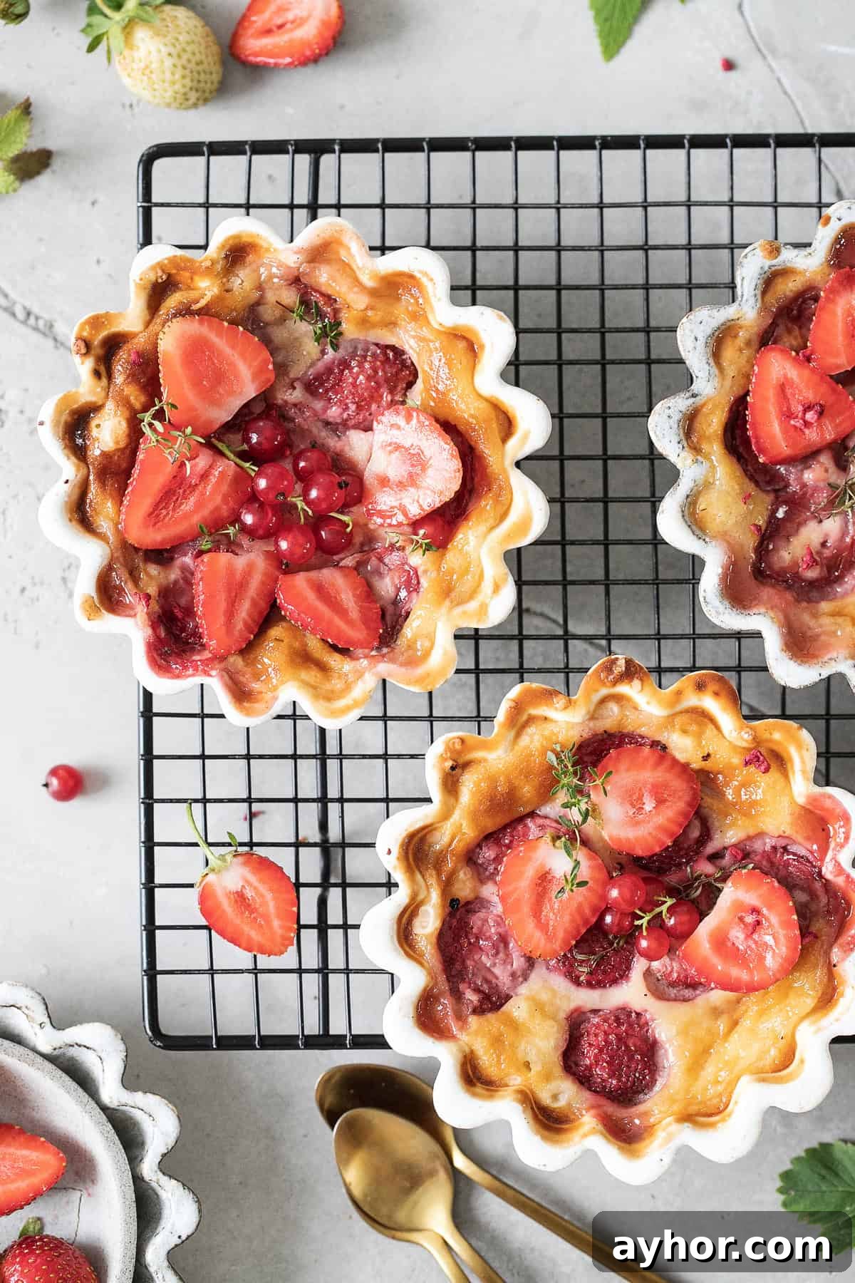 Freshly baked strawberry clafoutis in white ramekins cooling on a wire rack.