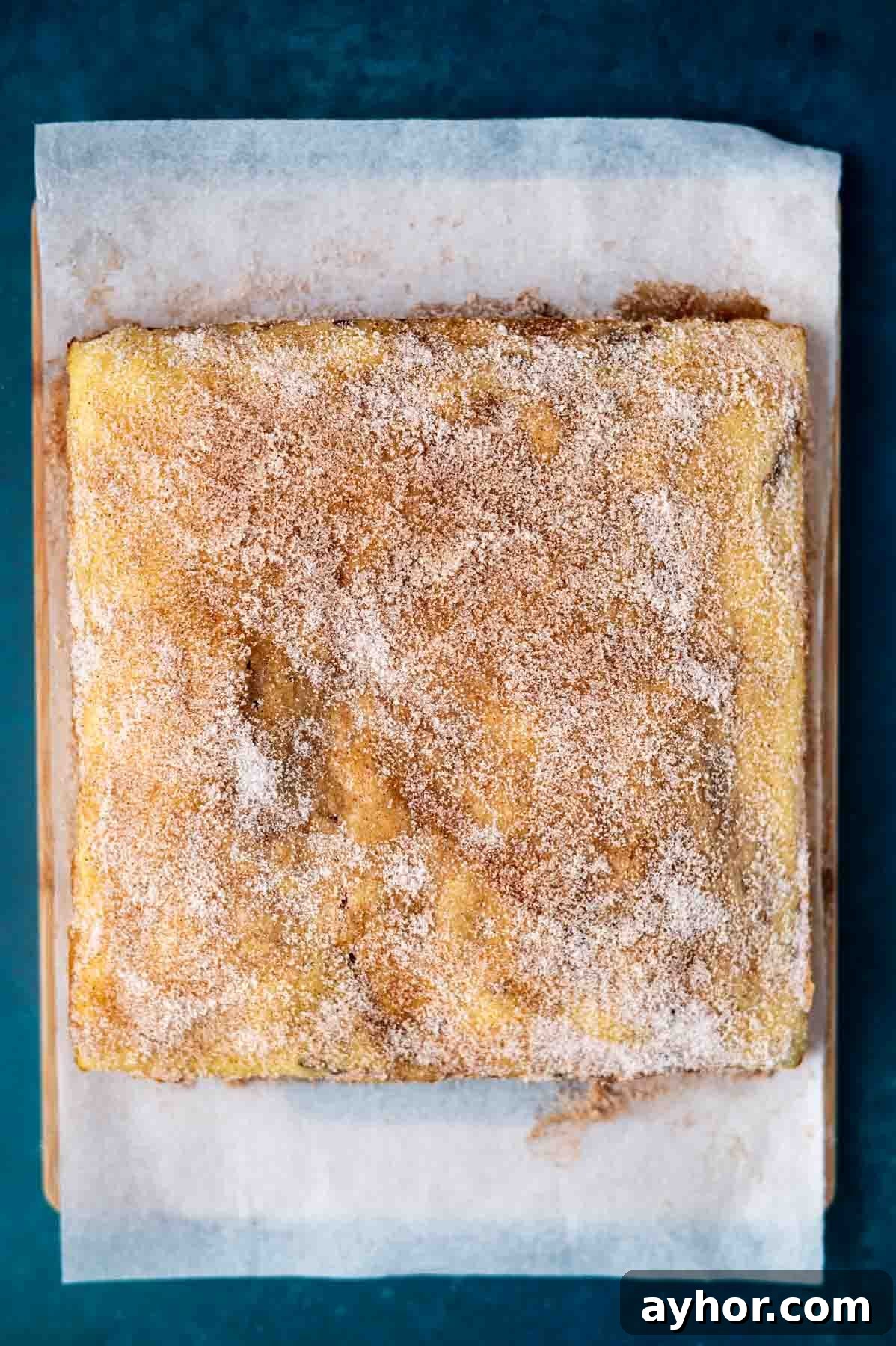 cinnamon sugar coating on top of a churro cake sitting on a parchment lined cutting board