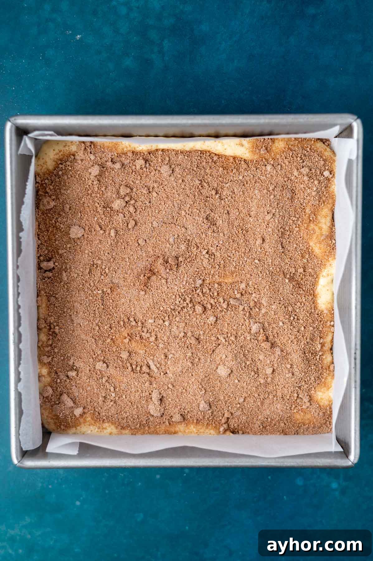 cinnamon filling sprinkled over cake batter in a parchment lined baking pan
