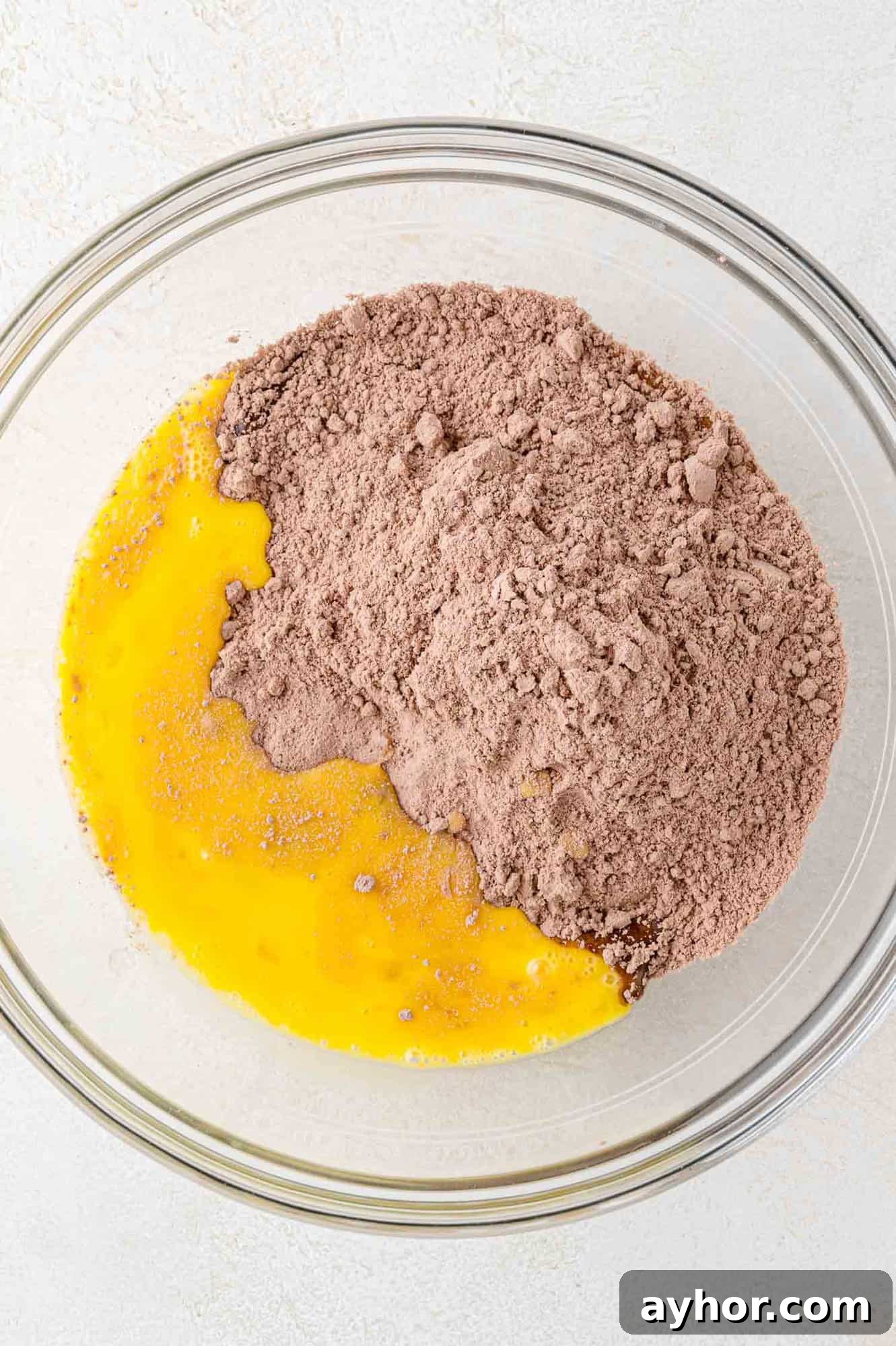 A glass bowl containing beaten eggs and dry chocolate cake mix, ready to be combined.