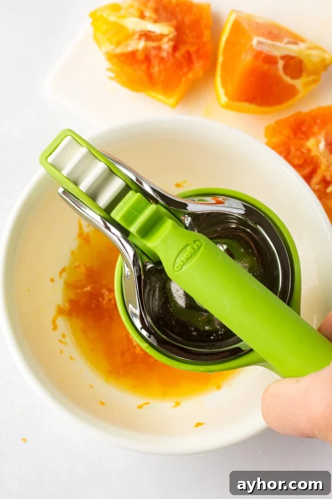 Honey Orange Vinaigrette with 6 Simple Ingredients 5 Juicing pieces of orange with a green handheld juicer over a medium white bowl.