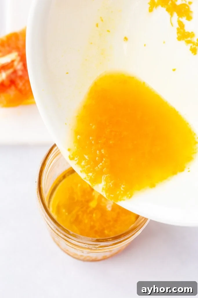 Honey Orange Vinaigrette with 6 Simple Ingredients 7 Pouring orange zest and juice out of a medium white bowl into a small mason jar.