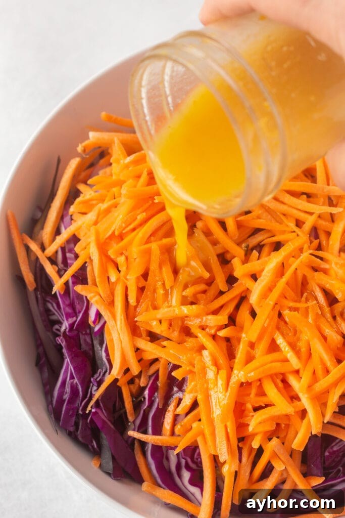 Honey Orange Vinaigrette with 6 Simple Ingredients 9 Close up of a hand pouring orange dressing out of a small mason jar onto a red cabbage and carrot slaw.