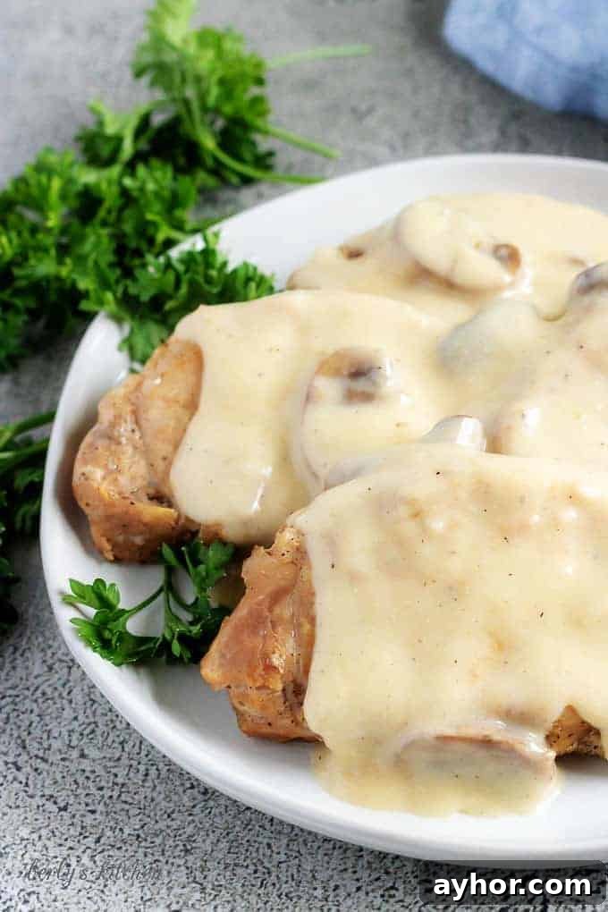 Instant Pot Pork Chops in Creamy Mushroom Gravy 7 A close-up photo of the Instant Pot pork chops, covered with gravy and being served on a whit serving platter.
