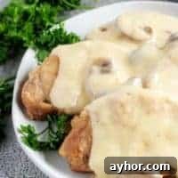 Instant Pot Pork Chops in Creamy Mushroom Gravy 8 A close-up photo of the Instant Pot pork chops, covered with gravy and being served on a whit serving platter.