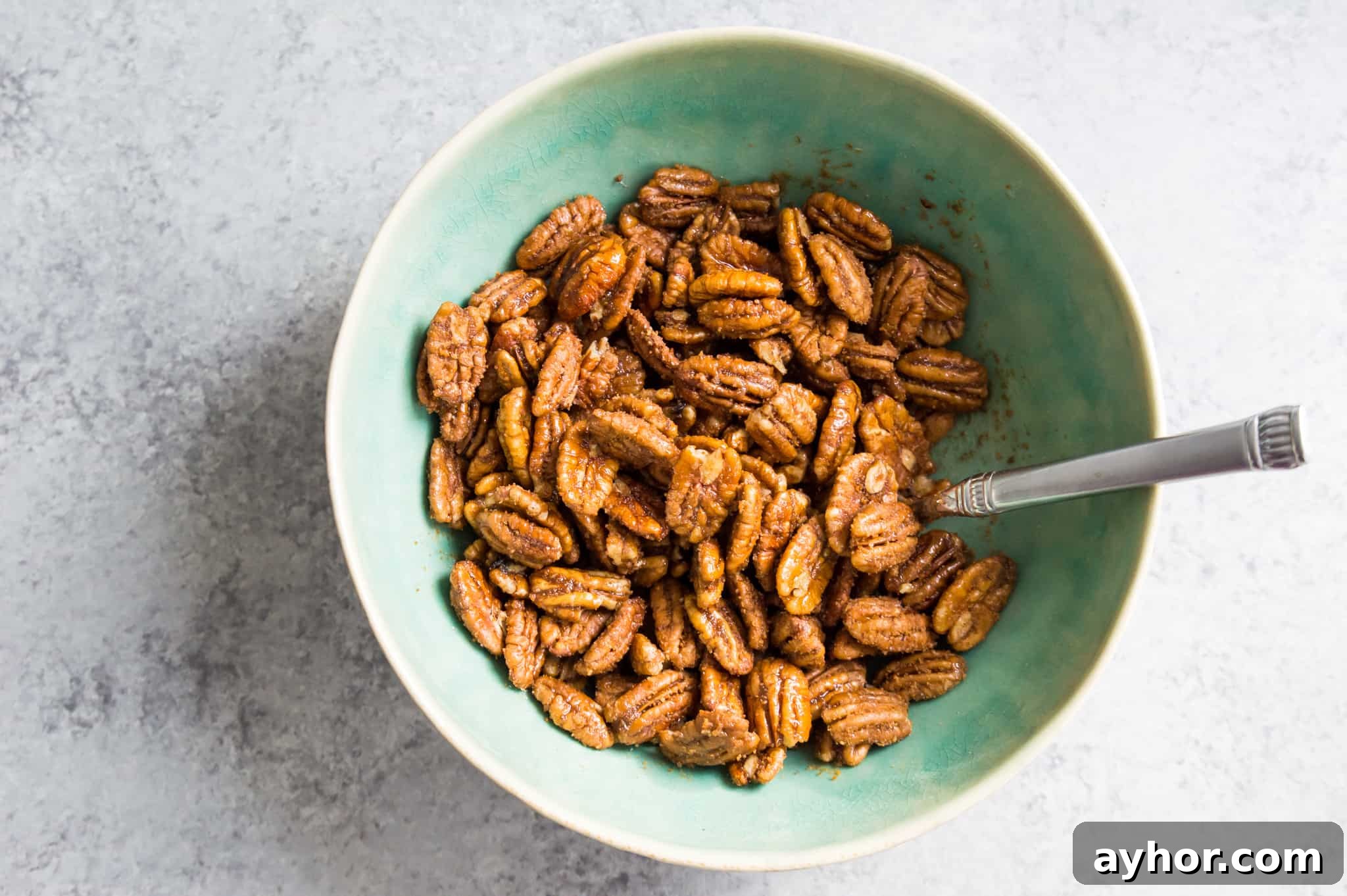 Homemade Chocolate-Covered Pecans: Simple No-Bake Recipe 4 A bowl of pecans covered in oil and sugar with a spoon in the bowl.