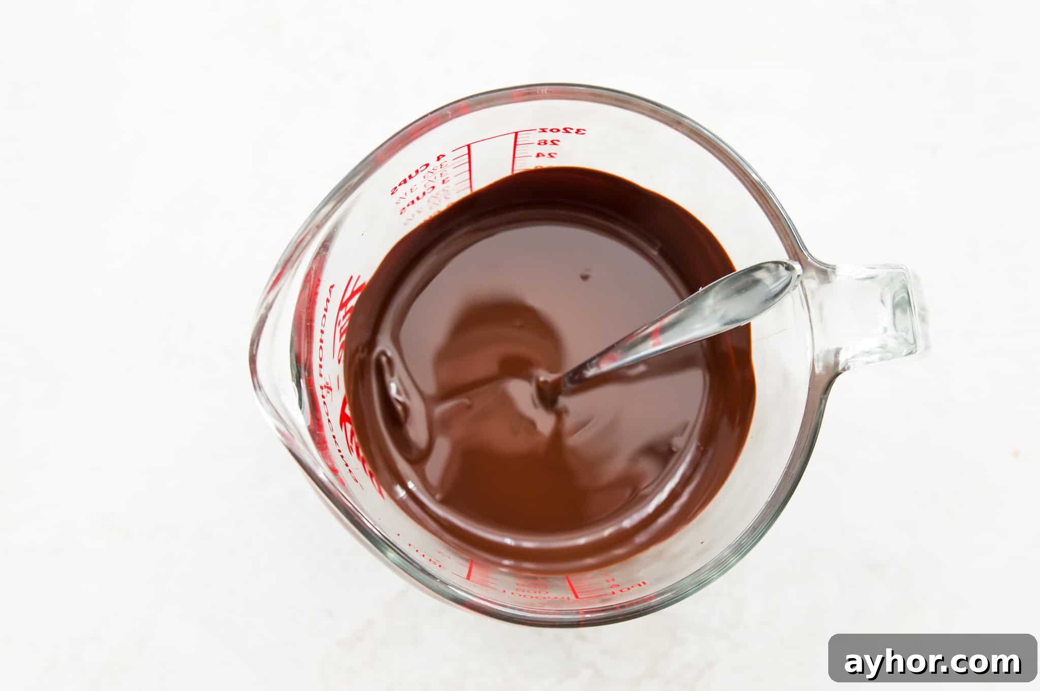 Homemade Chocolate-Covered Pecans: Simple No-Bake Recipe 6 A glass measuring cup with melted chocolate in it and a spoon in the chocolate.