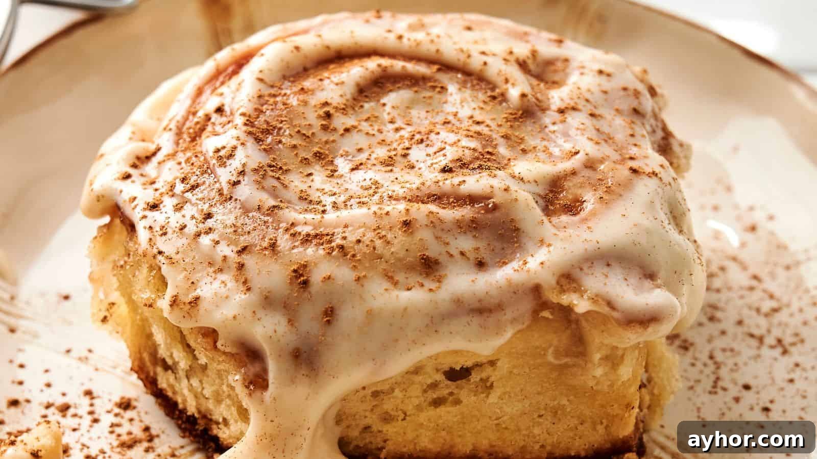 29 Breakfast Recipes to Make Your Mornings Feel Romantic 15 A close-up of a sourdough cinnamon roll topped with creamy icing and a sprinkle of cinnamon on a plate.