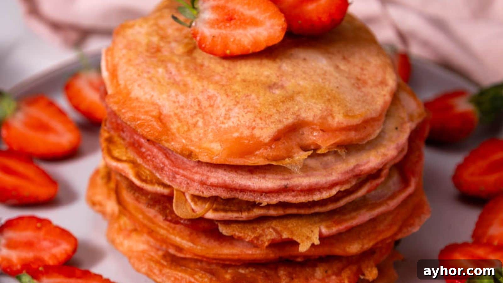 29 Breakfast Recipes to Make Your Mornings Feel Romantic 19 A stack of pancakes topped with sliced strawberries, surrounded by more strawberries on a plate.