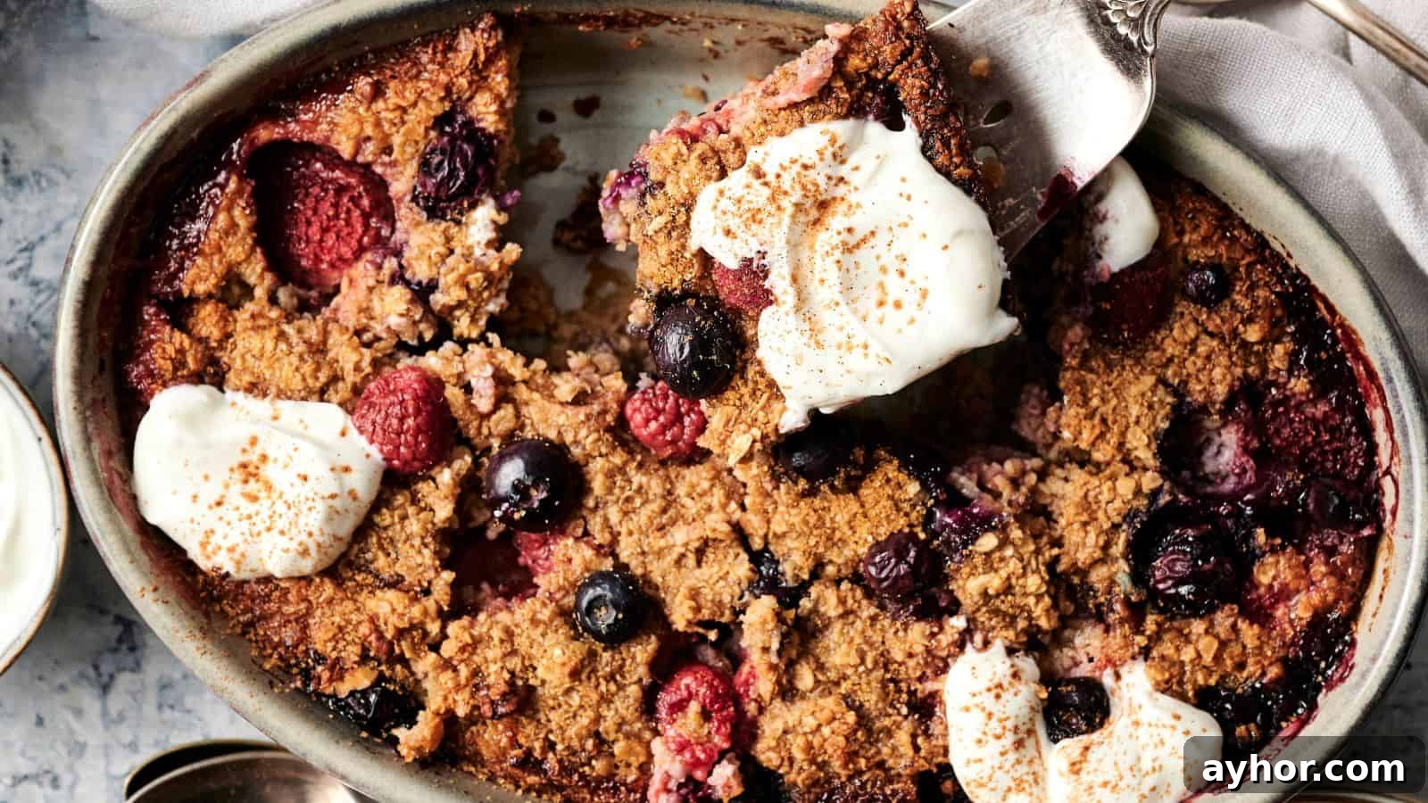 29 Breakfast Recipes to Make Your Mornings Feel Romantic 3 Baked berry oatmeal in an oval dish, topped with dollops of cream and sprinkled cinnamon, with a serving spoon lifting a portion.