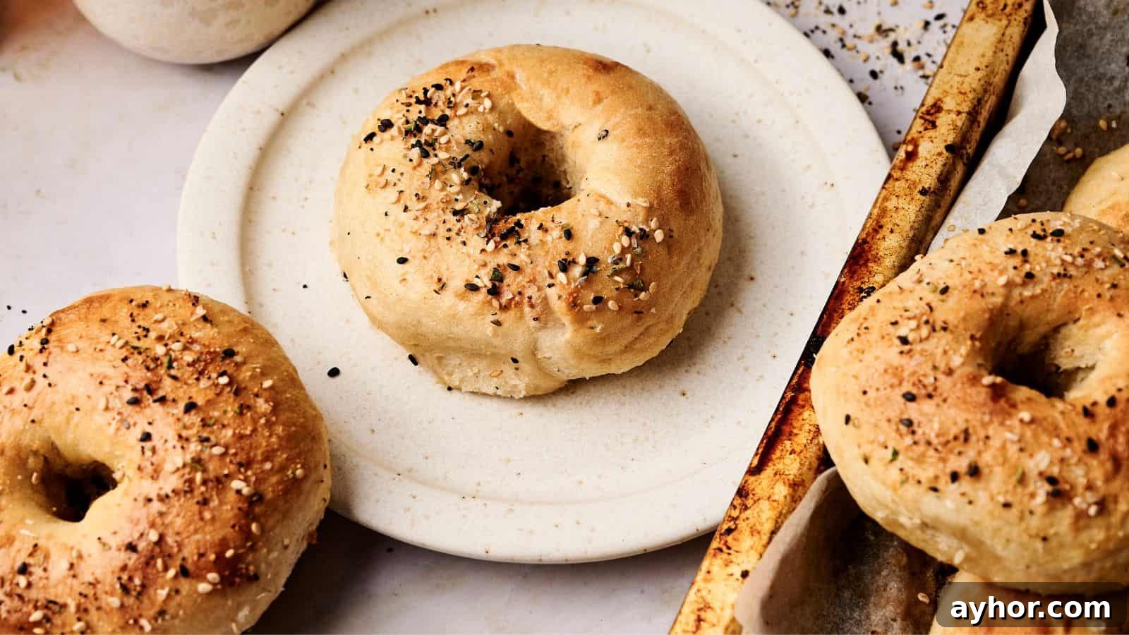 29 Breakfast Recipes to Make Your Mornings Feel Romantic 23 A plate with a bagel seasoned with seeds sits next to a baking tray holding more bagels, also topped with seeds.
