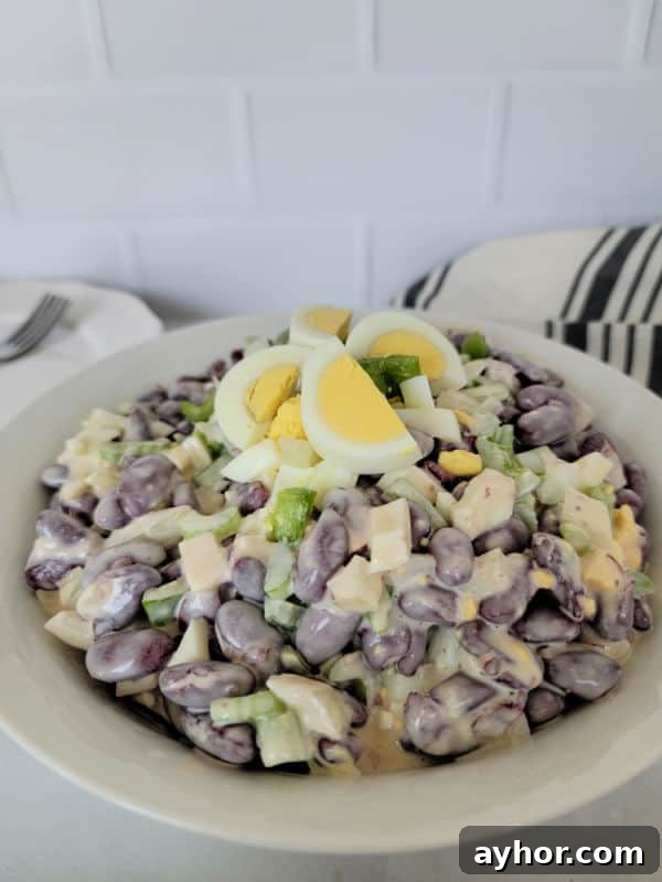 Hard boiled eggs cut into slices on kidney bean salad in a white bowl next to a cloth napkin