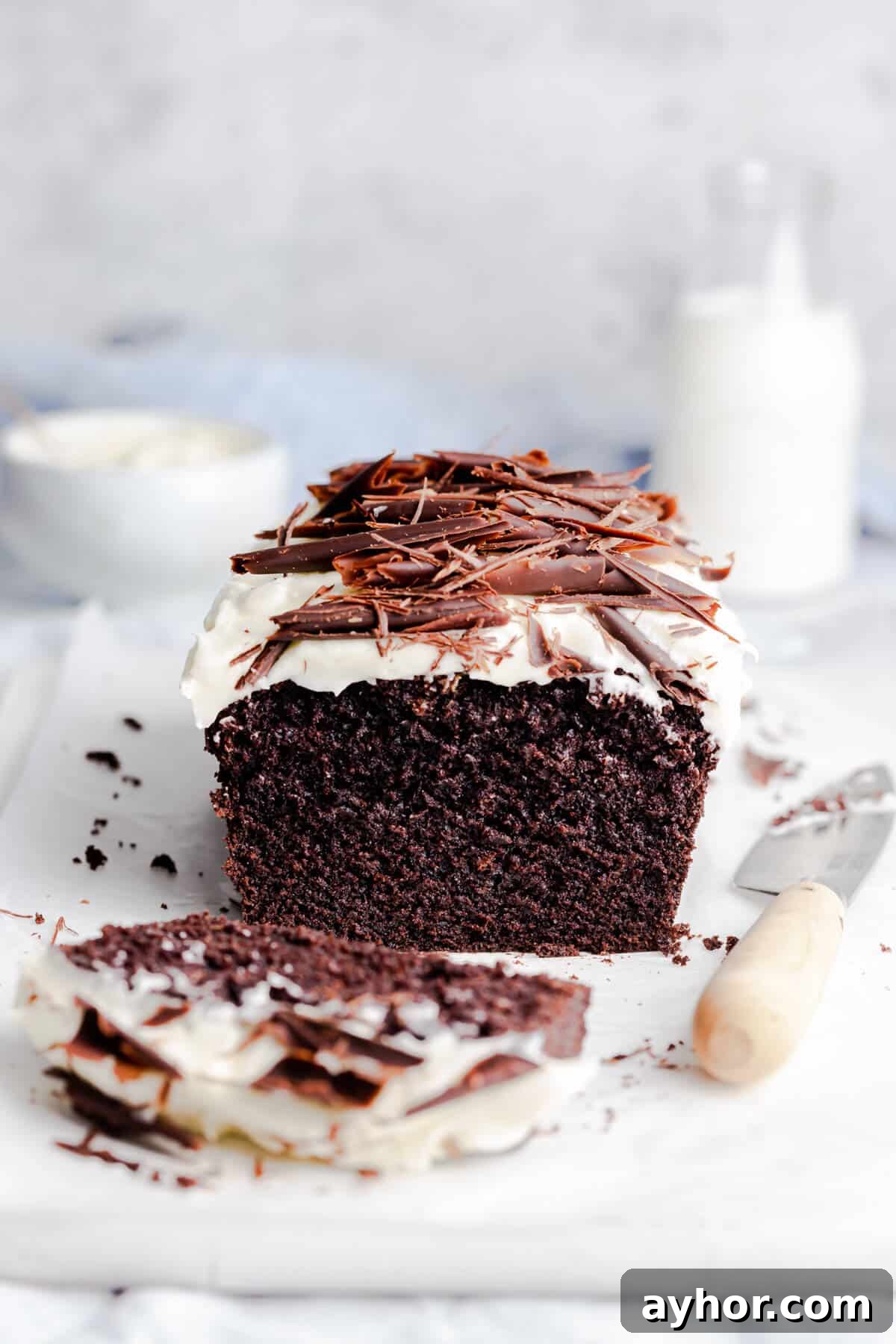 45 degree angle photo of chocolate loaf cake with frosting and with slice cut of