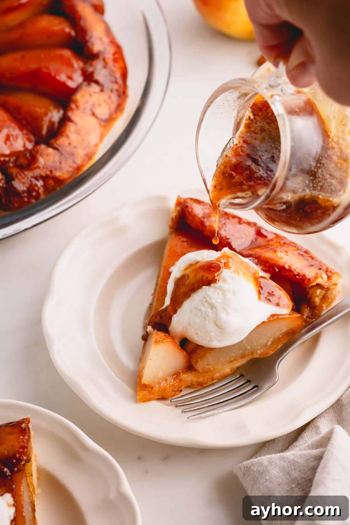 Pear syrup being poured over a slice of French pear pie topped with vanilla ice cream.