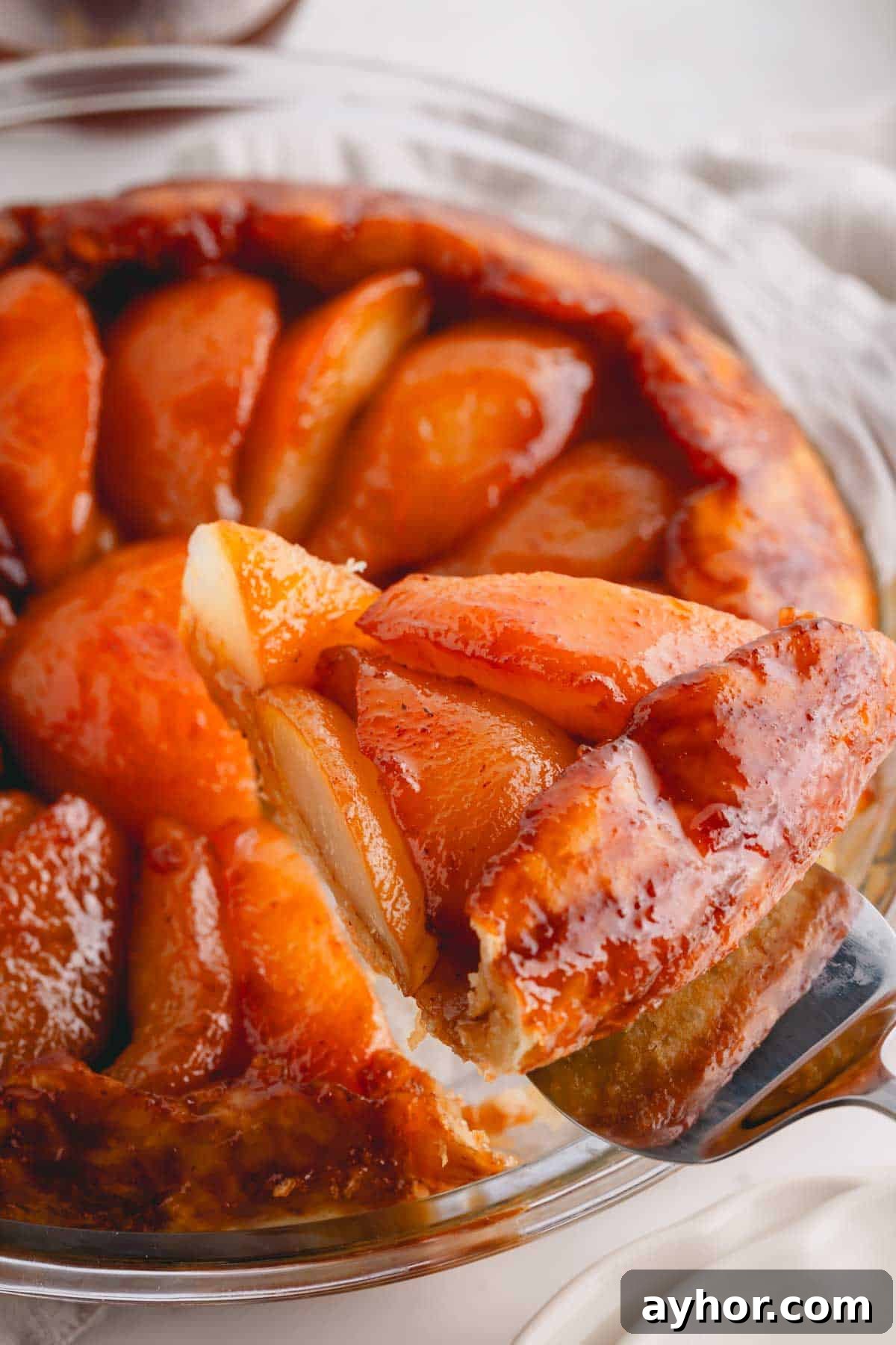 A slice of pear tarte tatin being lifted from a glass pie dish.