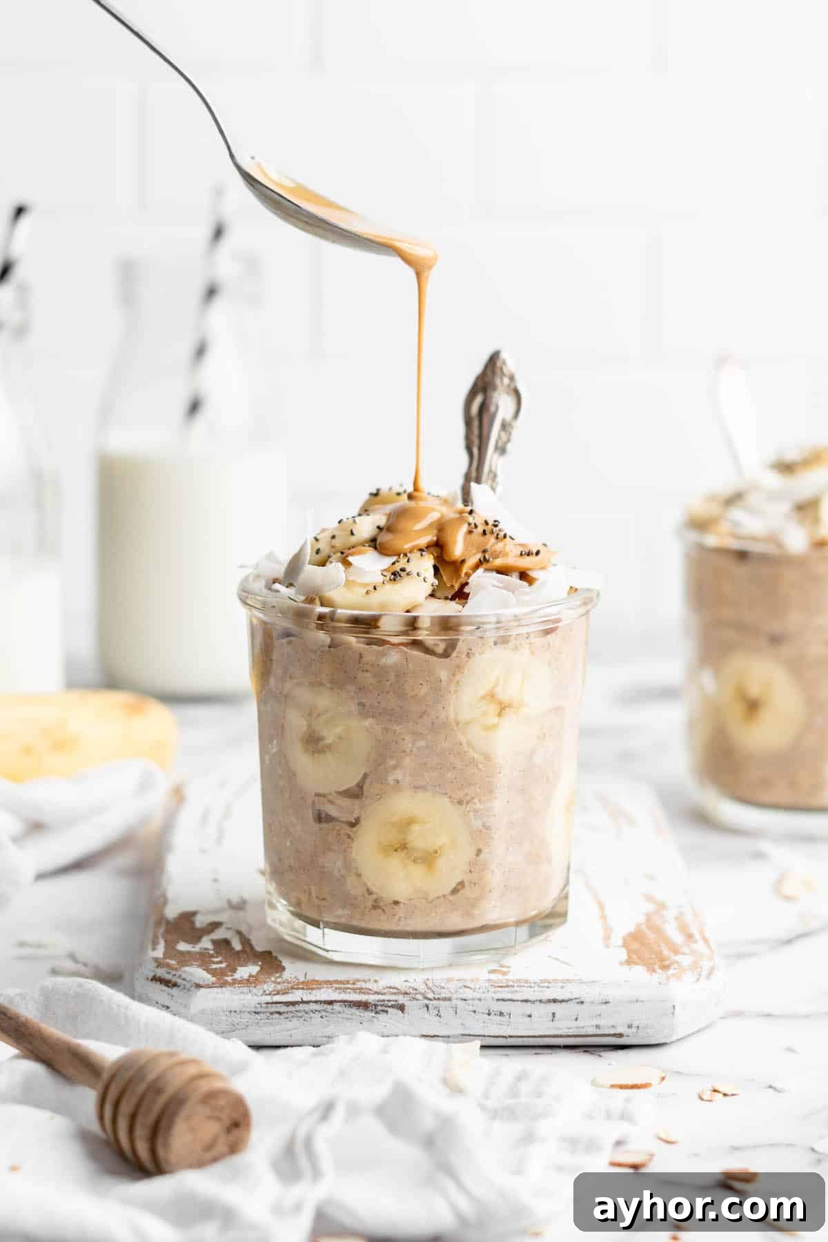 Spooning peanut butter over jar of overnight oats with bananas