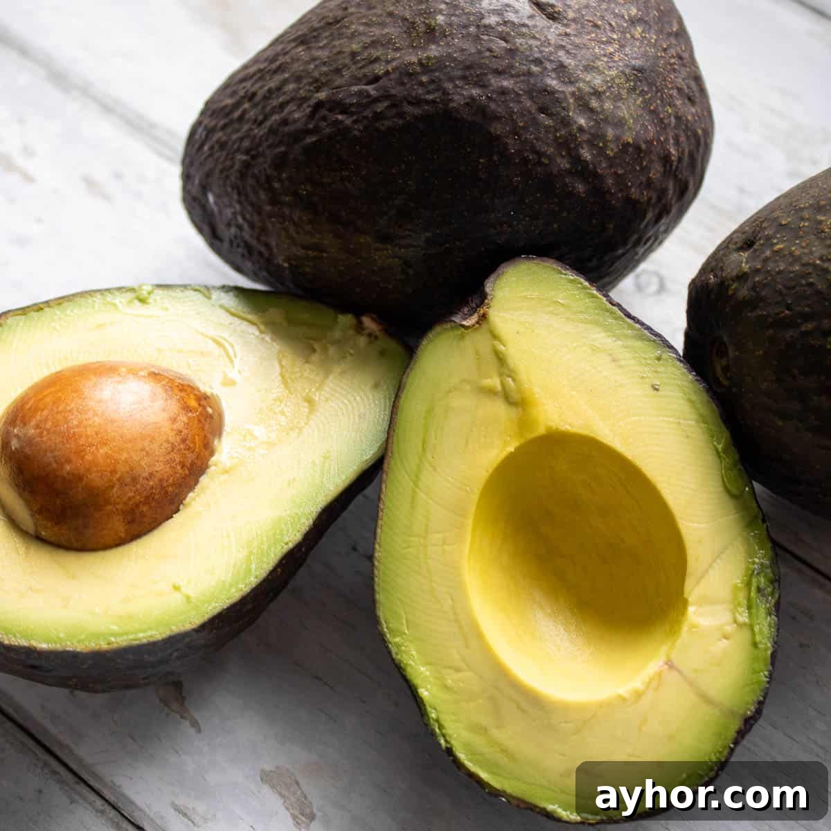 Half and whole avocado on a table.