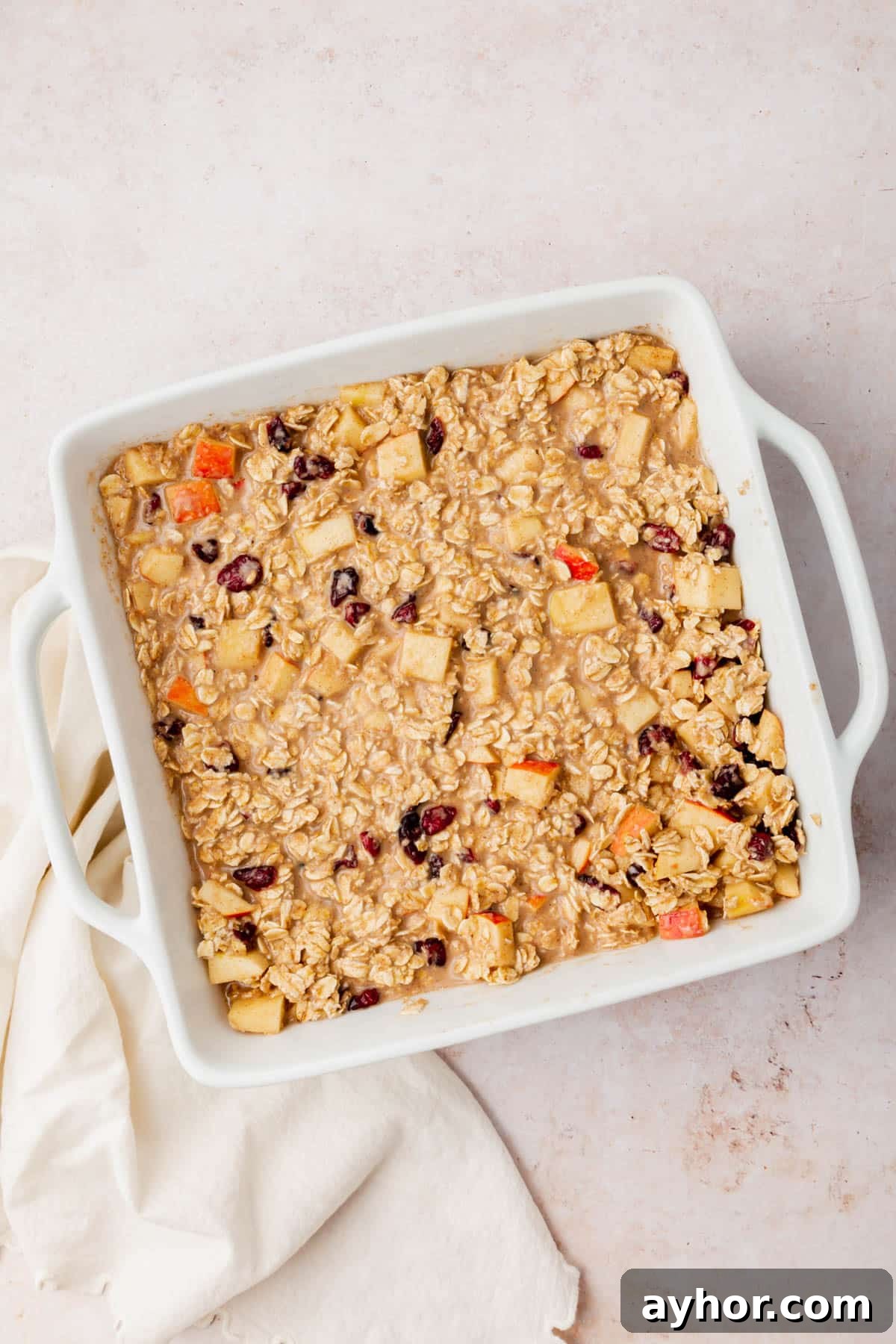An oatmeal, apple and dried cranberry mixture in a square baking dish before baking in the oven.