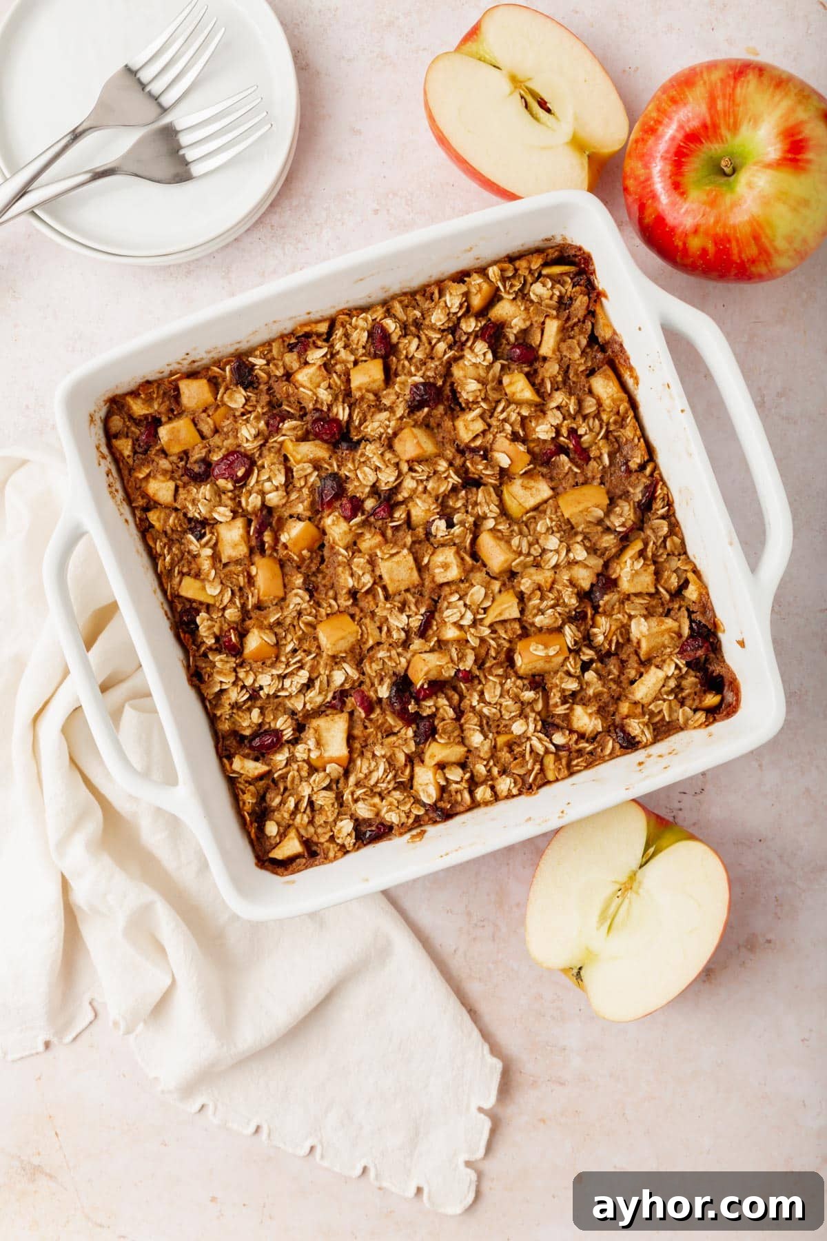 Gluten-free vegan apple baked oatmeal in a square baking dish with fresh apples surrounding the baking pan.