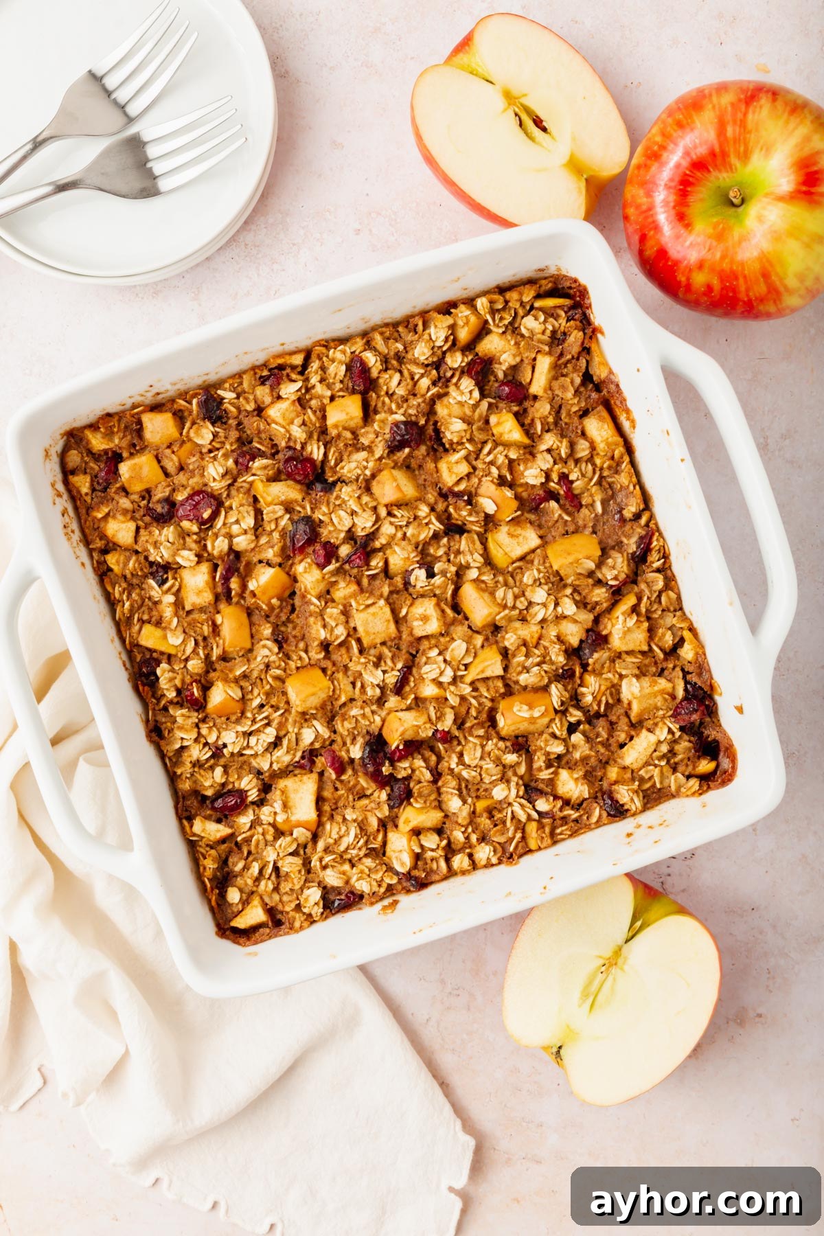 A tray of gluten-free vegan apple baked oatmeal next to a couple of apples on a table.