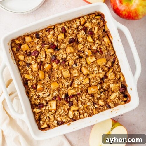 A tray of gluten-free vegan apple baked oatmeal next to a couple of apples on a table.