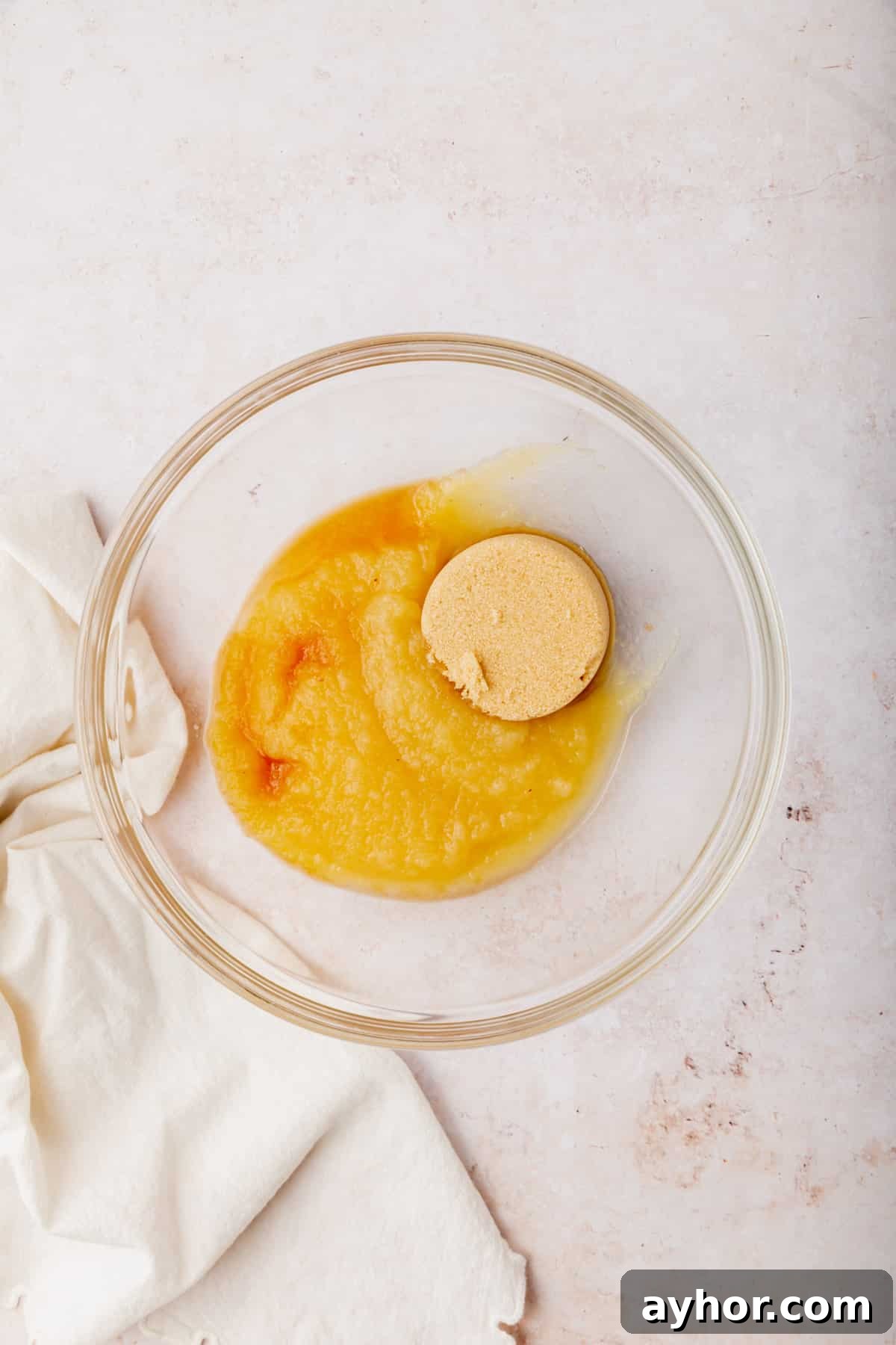 A glass mixing bowl with applesauce, brown sugar and vanilla in it before mixing together.