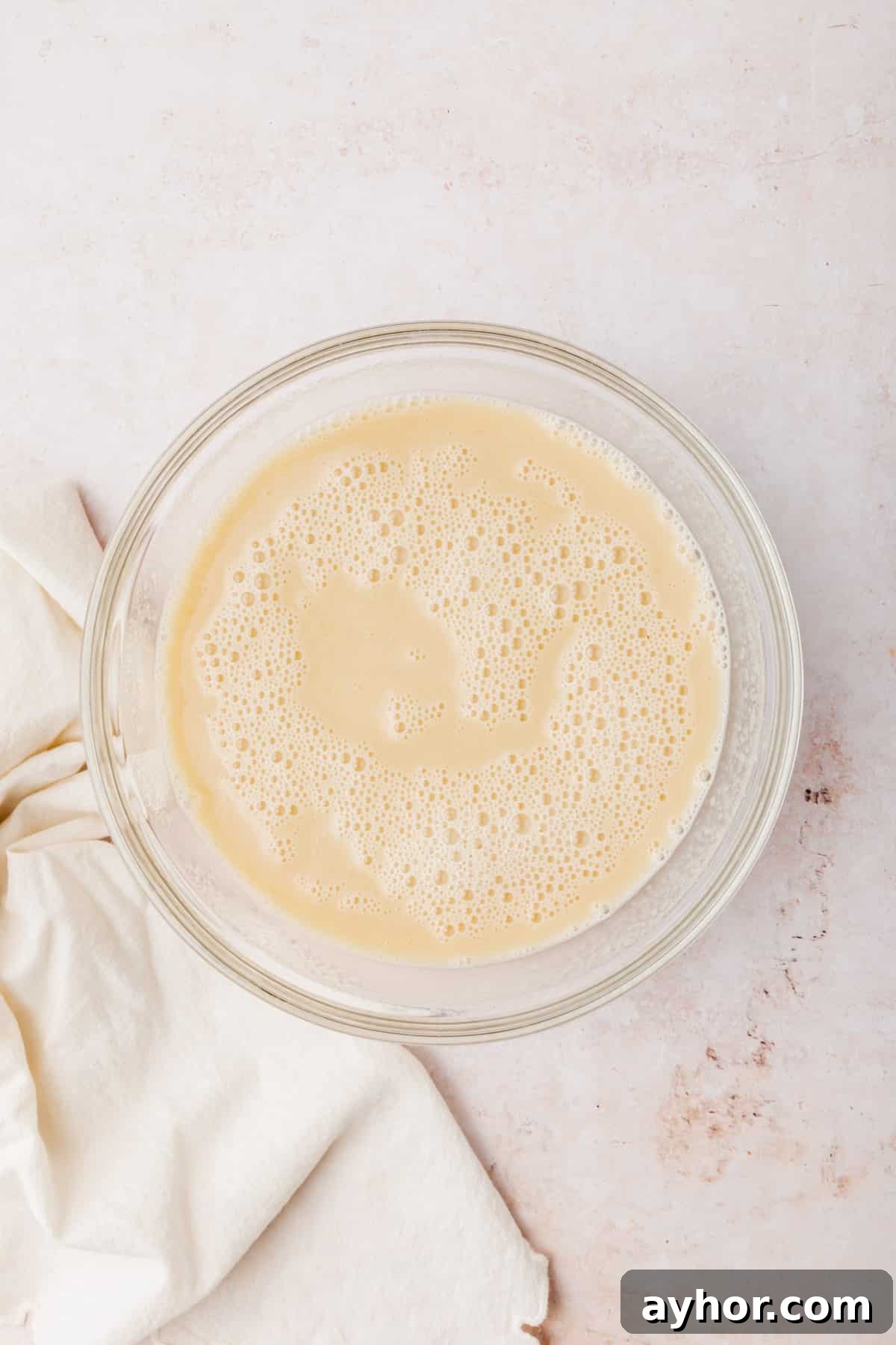 A glass mixing bowl with an almond milk mixture in it that has been mixed together.