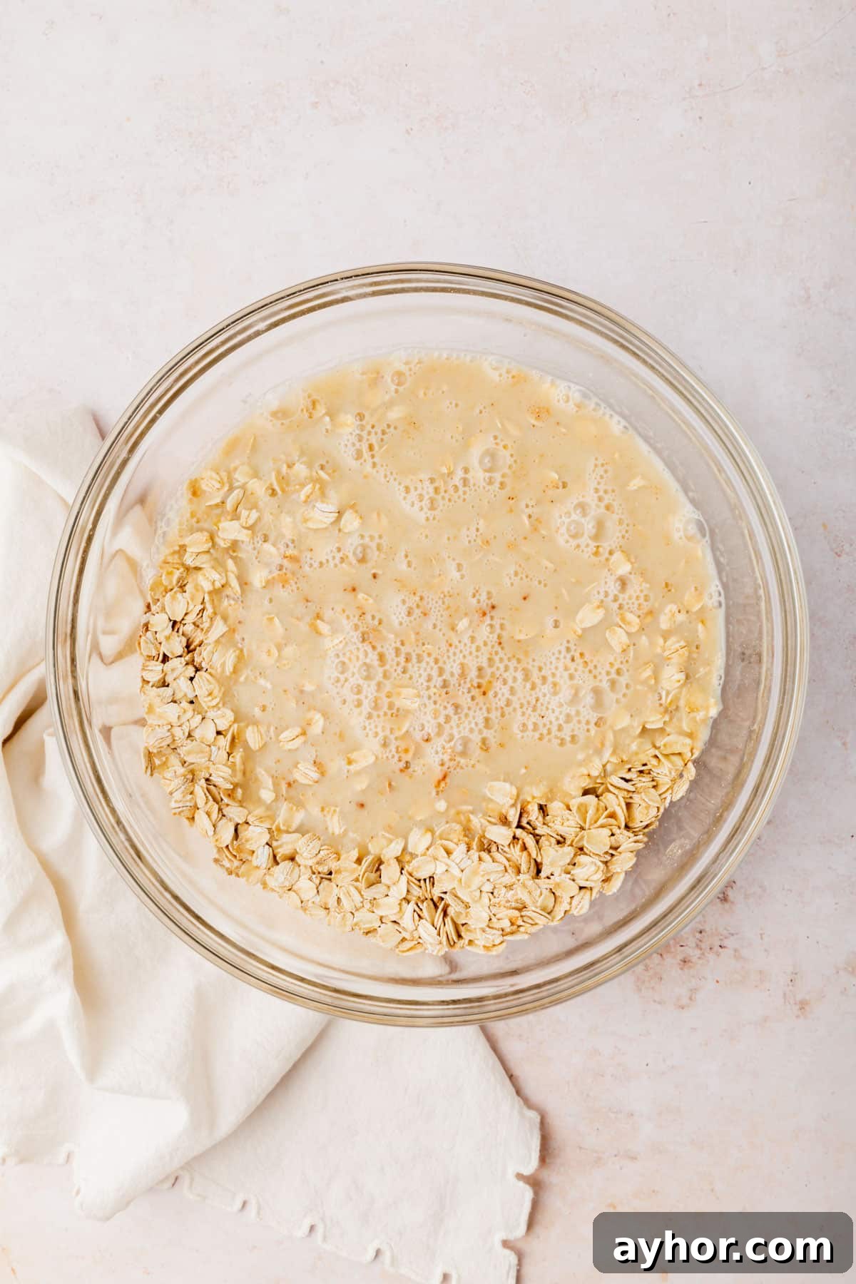 A glass mixing bowl with gluten-free oats topped with an almond milk mixture before mixing together.