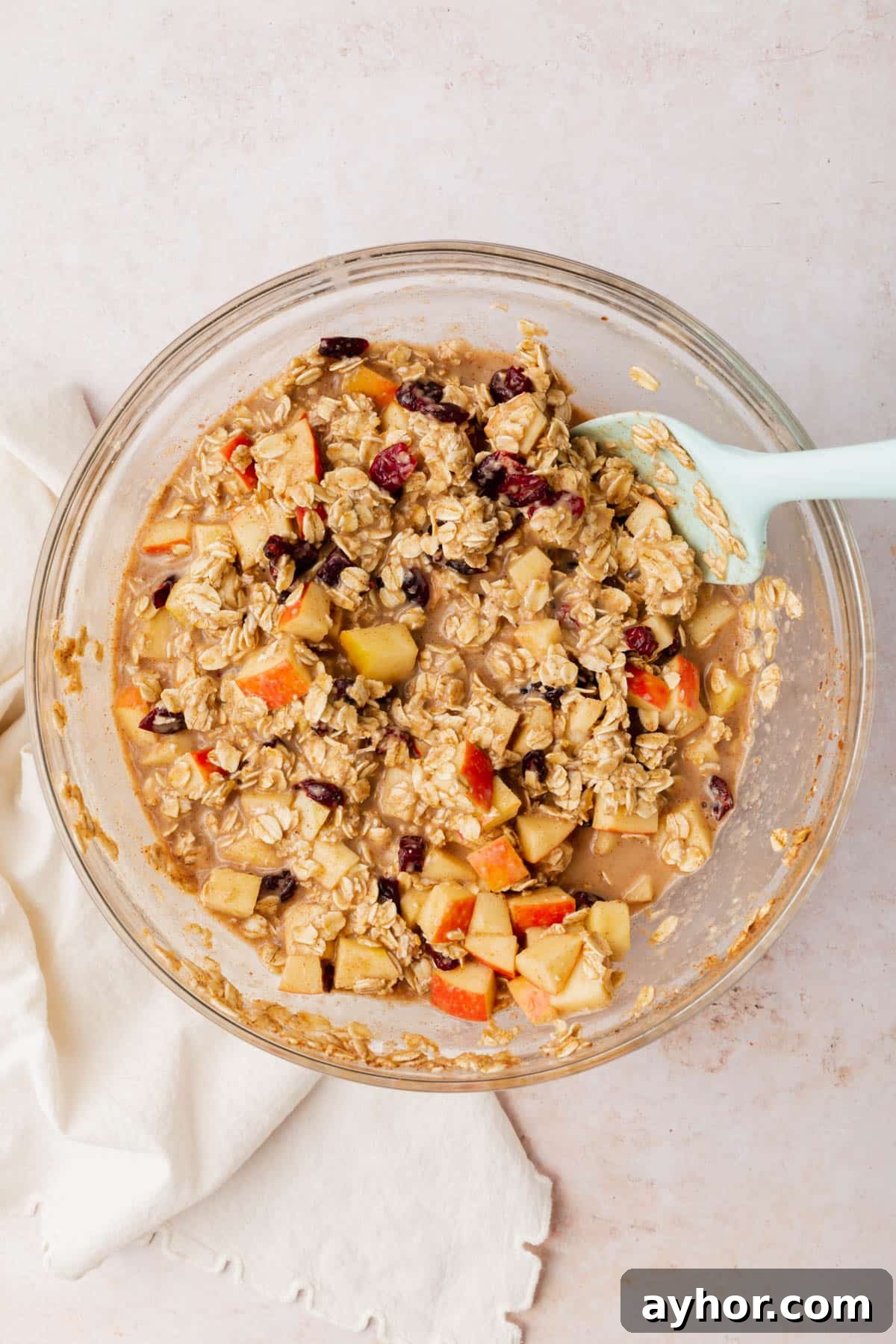A glass mixing bowl with an oatmeal, apple and dried cranberry mixture in it.
