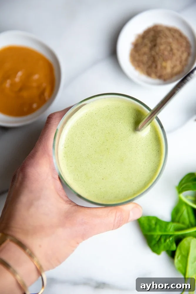 Low-Sugar Green Smoothie Recipe That Actually Tastes Great 4 Hand holding a green smoothie in a glass with a metal straw.