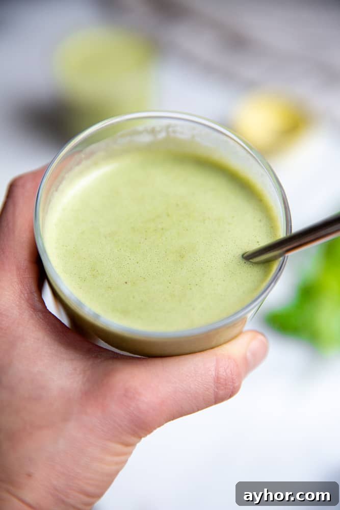 Low-Sugar Green Smoothie Recipe That Actually Tastes Great 9 Close up of a hand holding a green smoothie in a glass with a metal straw.