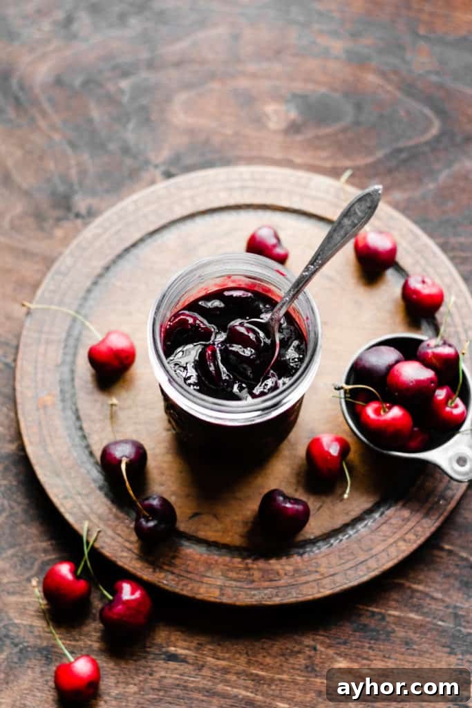 No-Bake Black Forest Chocolate Cherry Pie Recipe 5 A jar of homemade cherry sauce on a wooden surface, surrounded by fresh cherries