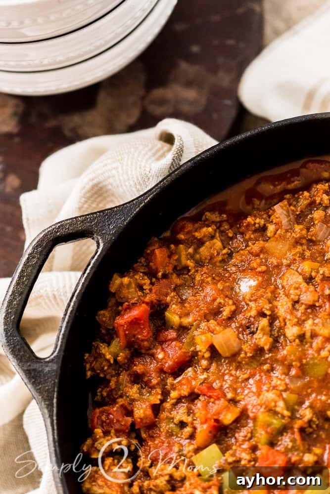 All-Meat Keto Chili Recipe (THM-S Friendly) 2 Overhead view of a cast iron dutch oven filled with an all meat chili without beans on a table with bowls and spoons