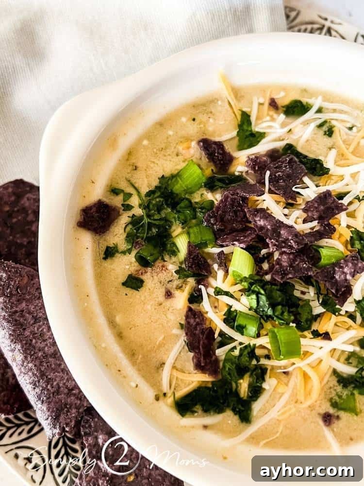 All-Meat Keto Chili Recipe (THM-S Friendly) 9 Crock of low fat healthy white chicken chili garnished with fresh cilantro, cheese, green onions on a plate with blue tortilla chips.