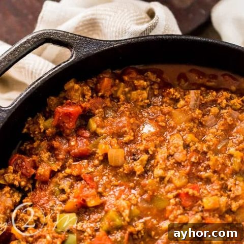 Overhead view of a cast iron dutch oven filled with an all meat chili without beans on a table with bowls and spoons
