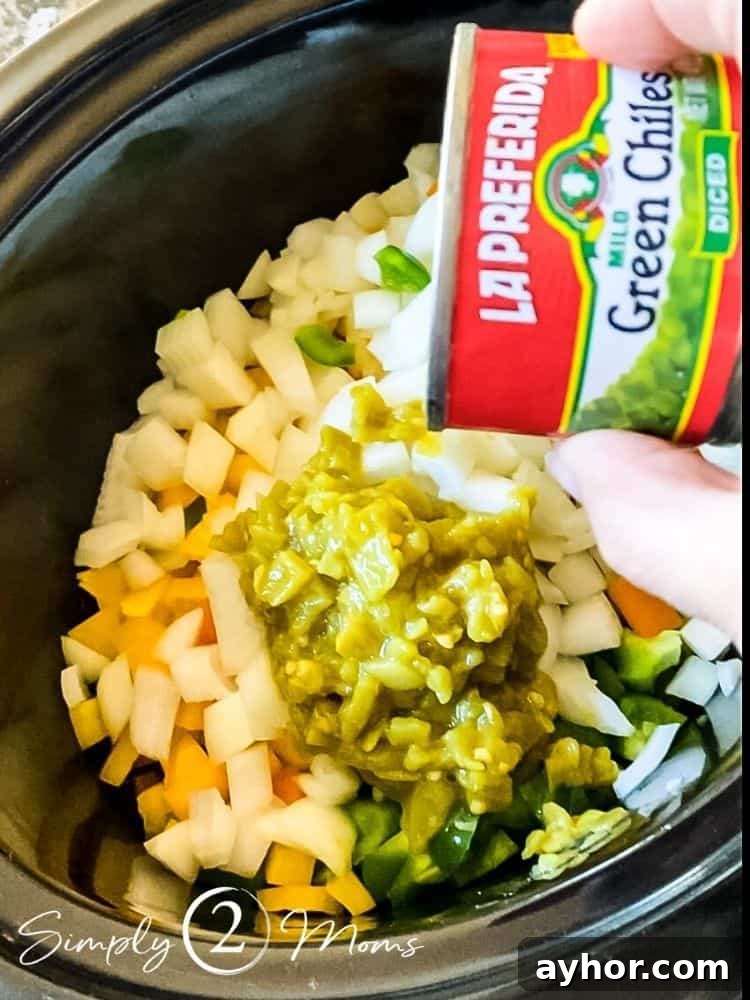 All-Meat Keto Chili Recipe (THM-S Friendly) 5 Crockpot with peppers and onions and a hand pouring in a can of green chiles