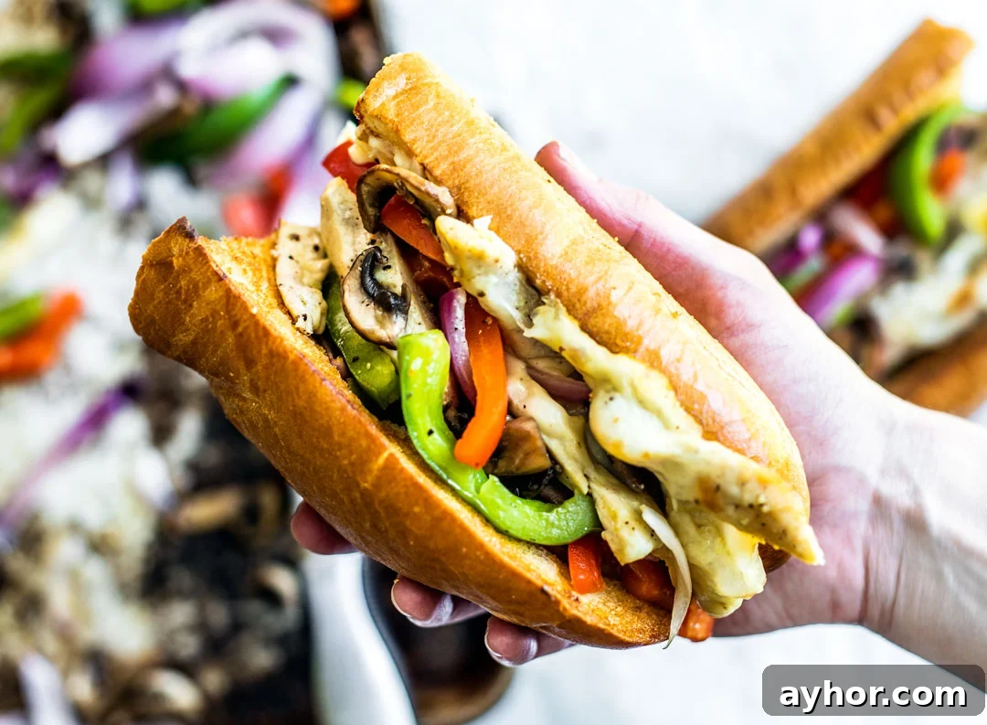 Hand holding out a Chicken Philly Cheesesteak sandwich.