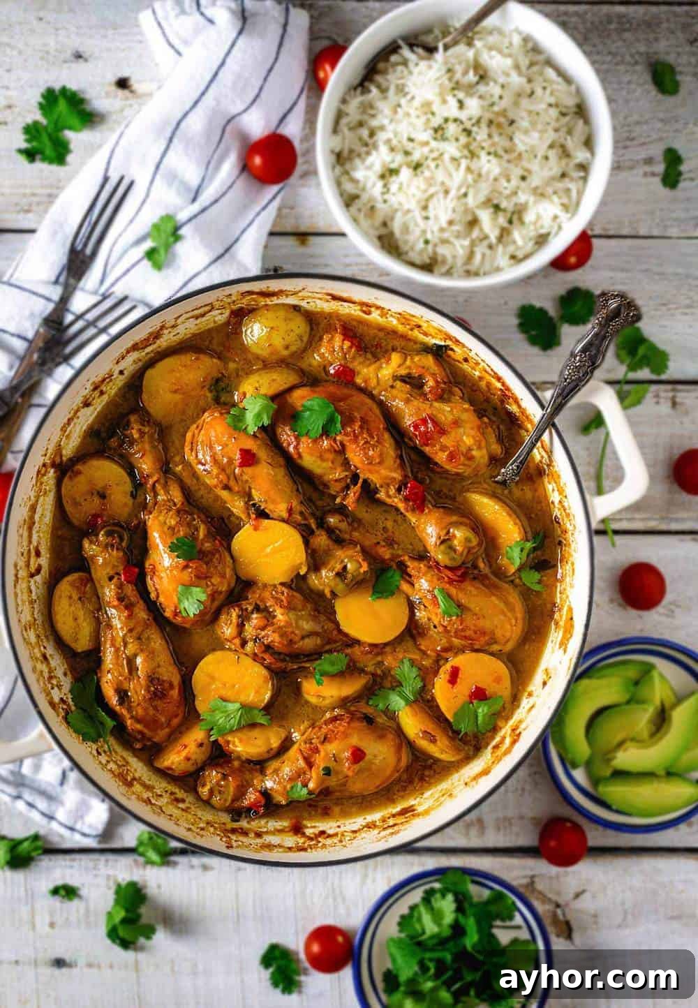 A Dutch oven with Colombian chicken and potato stew with rice and avocado servings on the table.