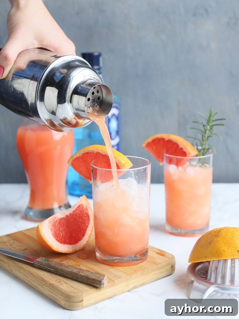 77 Brunch Cocktails to Impress Your Guests 4 hand pouring a grapefruit cocktail from a shaker into a glass garnished with a grapefruit wedge and a sprig of rosemary